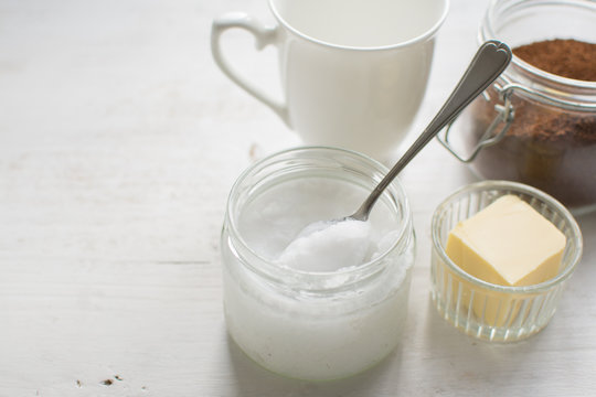 Ingredients for paleo style and ketogenic bulletproof coffee: coconut oil, butter, coffee on the white wooden table, copy space for text, selective focus