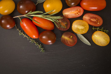 Colorful cherry tomatoes with herbs, on black background.