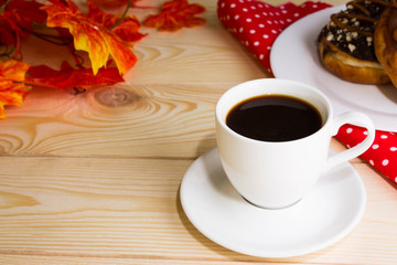 A cup of coffee with a chocolate donuts and autumn leaves