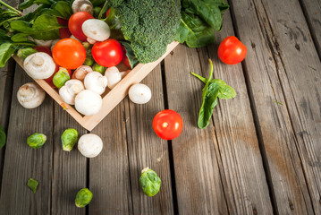 Fresh raw organic vegetables on a rustic wooden table in basket: spinach, broccoli, Brussels sprouts, tomatoes, mushrooms, champignons. Copy space
