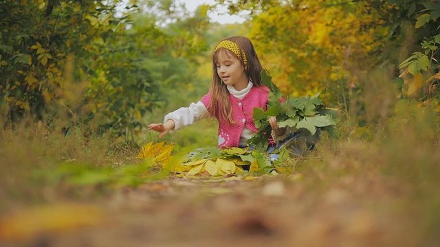 cheerful girl sitting on the footpath and throwing autumn leaves. Slow-motion