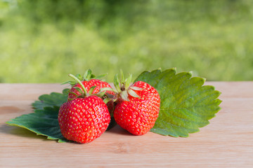 Ягоды и листья клубники на деревянном столе на фоне газона