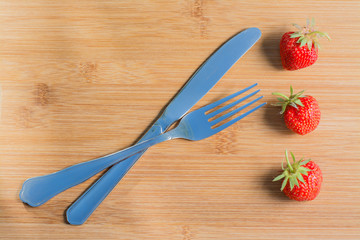 Ягоды клубники и столовые приборы на деревянном фоне