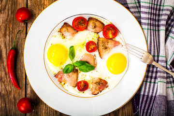 Fried eggs with bacon and vegetables on a white plate