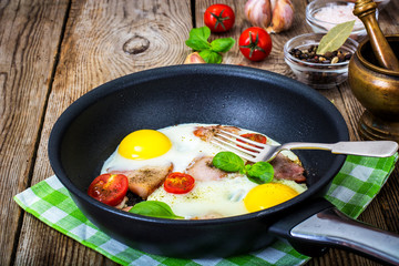 Fried eggs with bacon and tomatoes in a pan