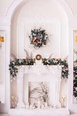 Classical fireplace with white clocks decorated with New Year tree branches. Christmas wreath hanging under it. Winter background. Vertical