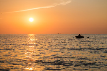 Закат на море, лодка с гребцом на фоне заката
