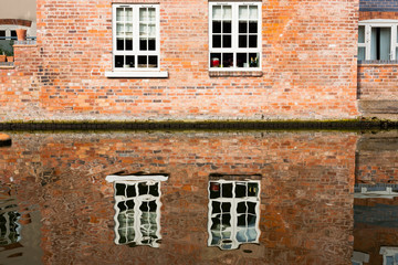 Fototapeta na wymiar Abstract water reflections of old red brick buildings with windows in canal on a sunny day in England UK