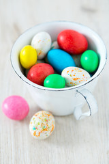 Fototapeta na wymiar Easter candy eggs in miniature cup on wooden surface