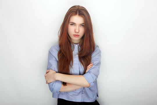 Young serious angry redhead beautiful woman in shirt portrait on a white background hugging herself