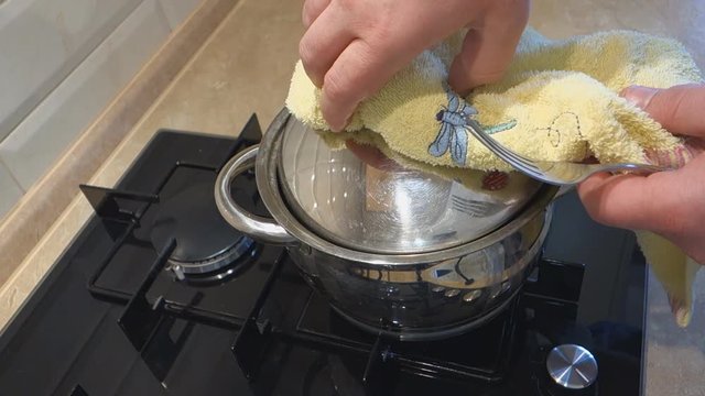 man comes to a gas stove and opens with a towel cover the pan