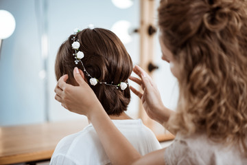 Female hairdresser making hairstyle to brunette girl in beauty salon.