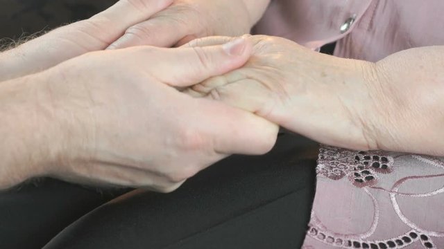 Man strokes the old woman's hands during illness