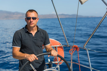 Male skipper at the helm sailing boat, controls ship during sea yacht race. Luxery vacations,...