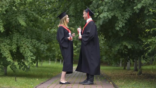 Smiling male and female graduates talking in park after graduation ceremony