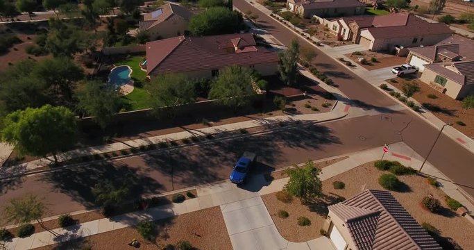 A flyover aerial establishing shot of a typical Arizona residential neighborhood as a vehicle leaves a driveway. Phoenix suburb.	 	