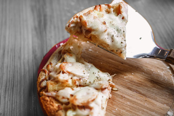 Hot pizza slice with melting cheese on a rustic wooden table.