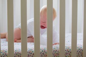 Baby boy crying in his cot refusing to sleep with a look of pure
