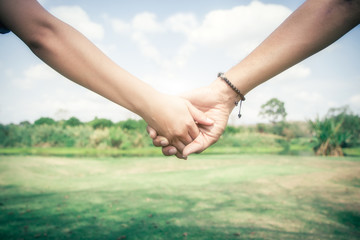 Valentine day background. Happy couple holding hands together as forever love with blurred greensward and blue sky. vintage color tone.