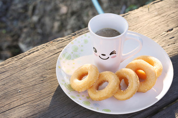 A cup of coffee and donuts on wooden table in the morning