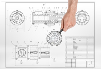 Male hand holding magnifying glass over detail drawing.