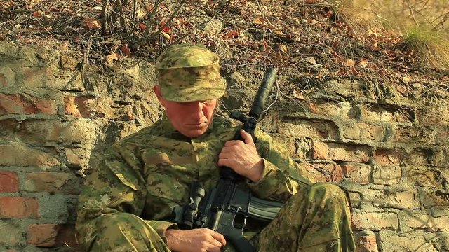 Soldier with automatic rifle  sleep and wake up near  brick wall 


