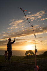 Father and daughter fly kite at sunset