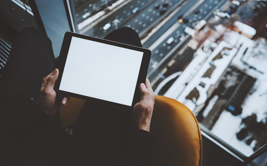 Close up view of mock up template of tablet pc in hands of man sitting near window of skyscraper,...