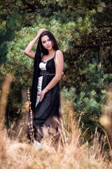 Graceful charming brunette model posing in black dress in coniferous park