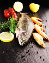 Delicious fresh fish on dark vintage background. Fish with aromatic herbs, spices and vegetables - healthy food, diet or cooking concept