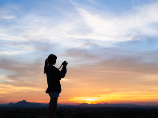 Silhouette of woman shooting with camera at sunset