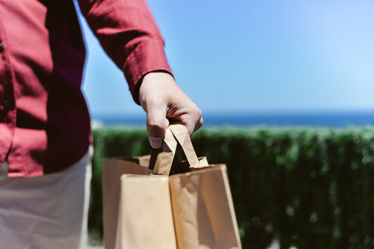 Closeup on person hand holding paper bag with handles, light background