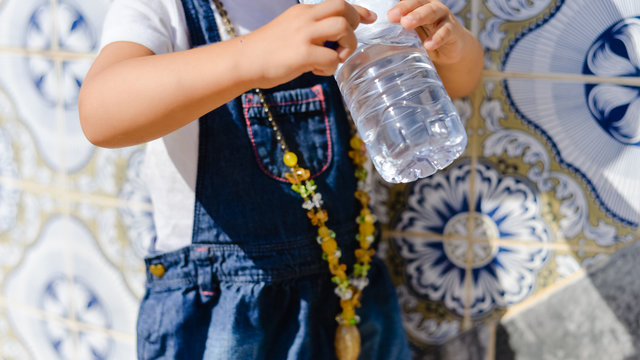 Closeup view of little child drinking water, hands holding bottle