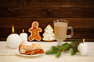 Gingerbread man and Christmas tree, cappuccino, fir twig, apple cake and candles on the wooden background