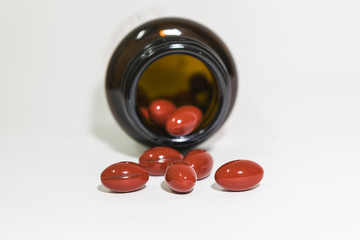 Red vitamin capsule from the bottle on white background