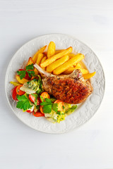 Grilled pork cutlet meat garnished with potato and salad on black table