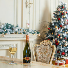 Bottle of white wine and glass on the table in beautiful holdiay decorated room for Christmas celebrations. New Year decorations.