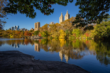 Fototapeta na wymiar Fall in Central Park at The Lake. Cityscape sunrise view with colorful Autumn foliage on the Upper West Side. Manhattan, New York City
