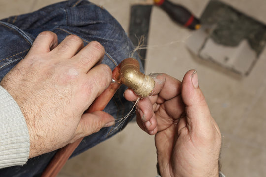 plombier installant radiateur avec tuyau de cuivre et joint filasse