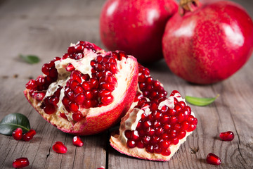 Whole and broken red ripe juicy pomegranates on rustic wooden unpainted table