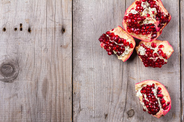 Broken red ripe juicy pomegranates on rustic wooden unpainted table
