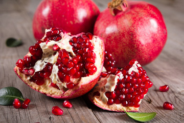 Whole and broken red ripe juicy pomegranates on rustic wooden unpainted table