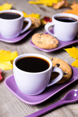 Purple coffee cup with saucer, spoon and Colourful fall leaves on gray wooden table background