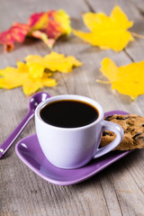Purple coffee cup with saucer, spoon and Colourful fall leaves on gray wooden table background