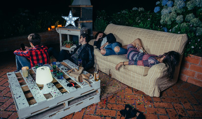 Young drunk friends sleeping in a sofa after outdoors party. Fun and alcohol and drugs problems concept.