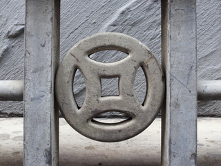 Close up on Chinese traditional totem shape railing. The shape symbolizes ancient Chinese coin which brings fortune and wealth. Grey color on grey wall background.