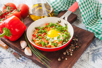fried eggs with a tomato and a paprika in a frying pan on a board, selective focus