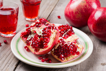 Whole and broken red ripe juicy pomegranates on rustic wooden unpainted table