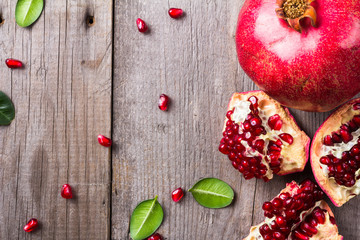 Broken and whole red ripe juicy pomegranates on rustic wooden unpainted table