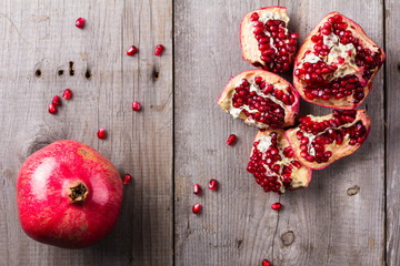 Broken and whole red ripe juicy pomegranates on rustic wooden unpainted table